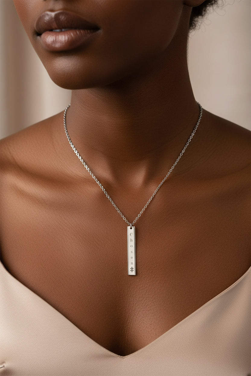 black woman wearing silver uncoated stainless steel necklace engraved with the word “Chosen” and a puzzle piece symbol, representing faith and autism parent strength.by motivated vision