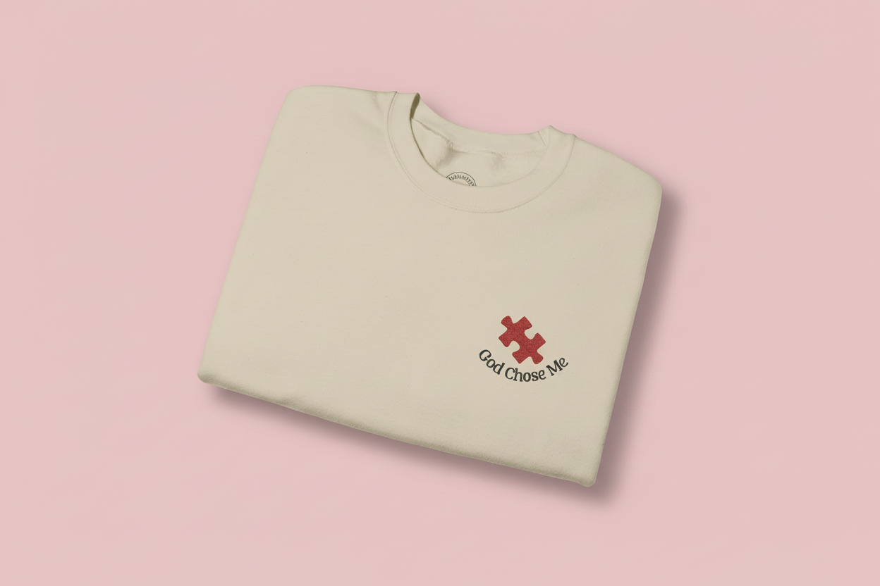 "God chose me" autism puzzle piece faith-based embroidery sweatshirt gildan 18000 sweatshirt sand. folded on pink background